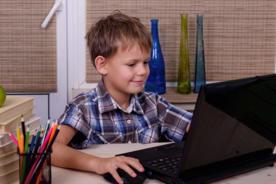 Young boy sitting at a desk using a laptop.