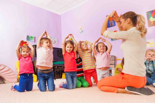 Five children and female teacher with arms raised playing a classroom game