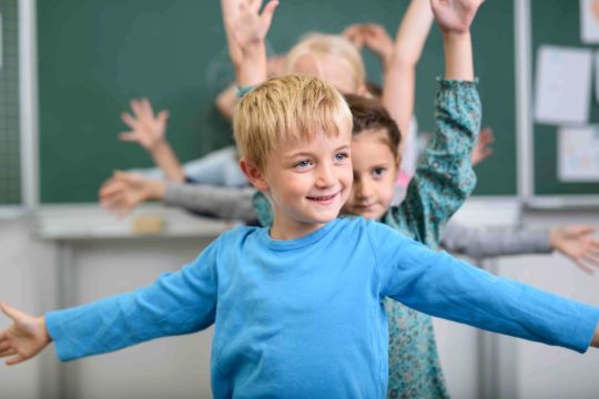 Young students standing doing a stretching exercise in classroom