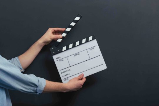 Male standing in front of a chalkboard holding a clapperboard