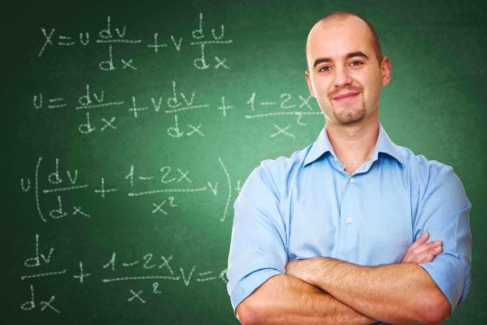 Male teacher with arms folded standing in front of a chalk board