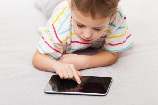 Young boy laying on his stomach playing on a tablet