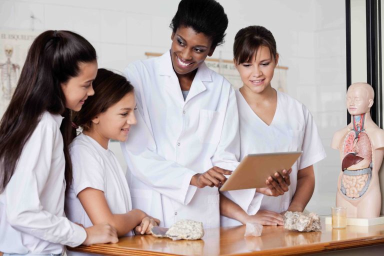 Female biology teacher holding tablet helping a group of students