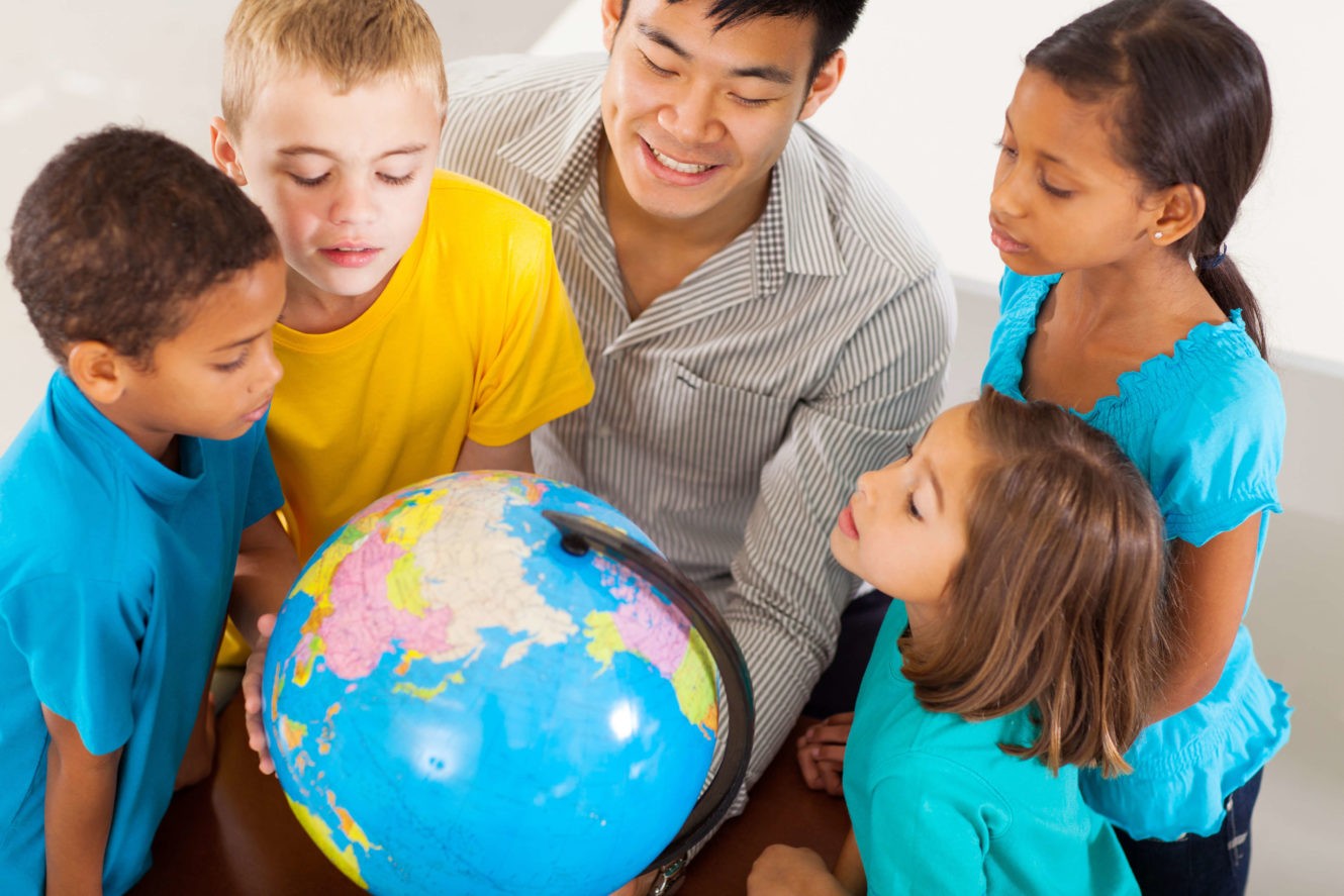 Male teacher and young students huddled around a globe